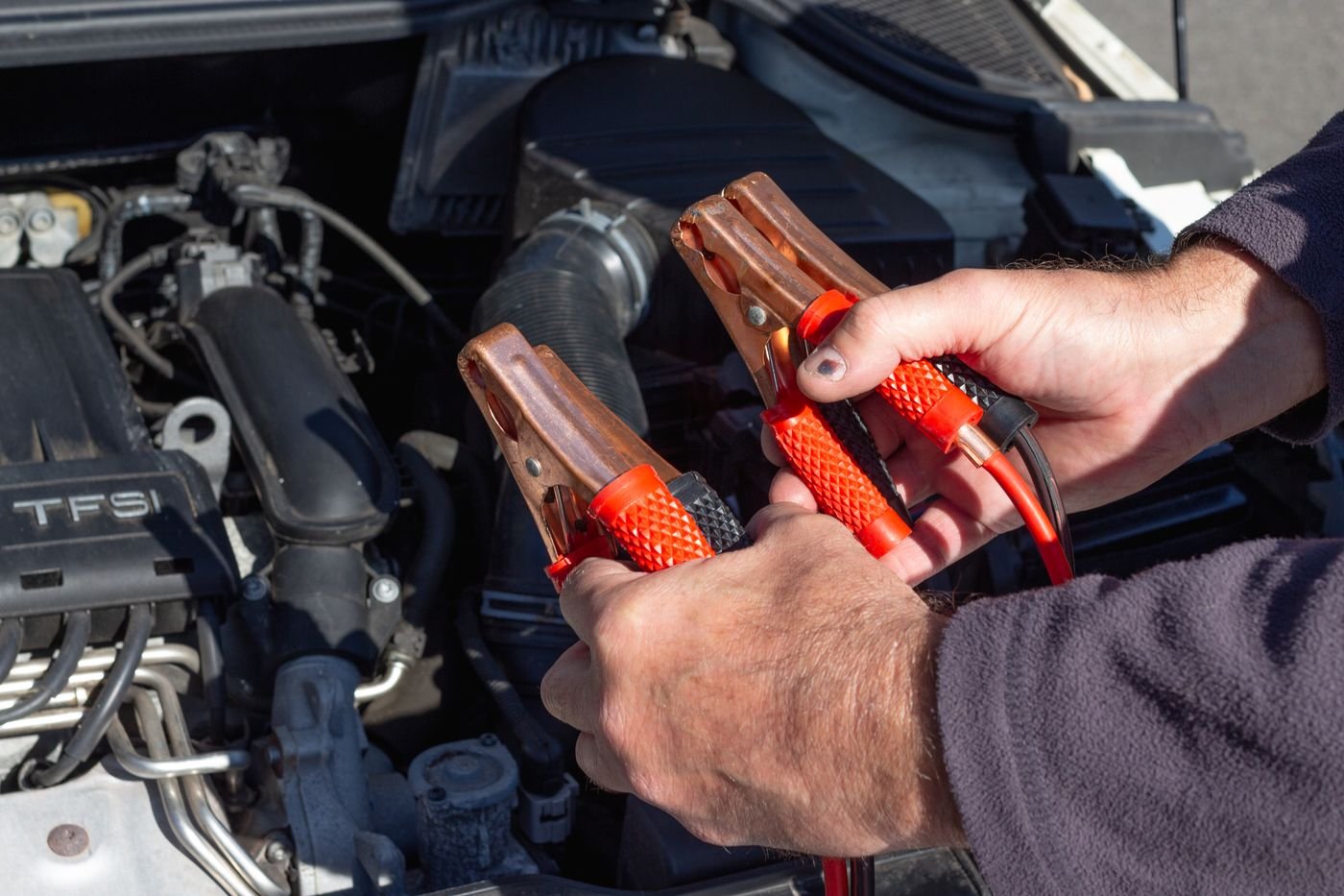 Hands holding jumper clamps over a car engine bay